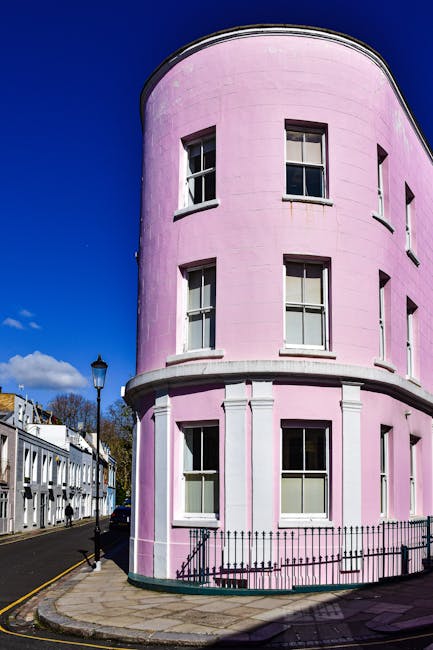 A close-up view of a pink residential building's exterior featuring a central dark blue front door with a brass mail slot and door knocker, accessed via a short set of concrete steps with metal handra