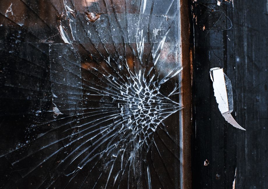 Close-up of a damaged wall with peeling blue and gray paint revealing the underlying plaster surface. The paint has cracked and curled away from the wall in irregular pieces, some with jagged edges, i